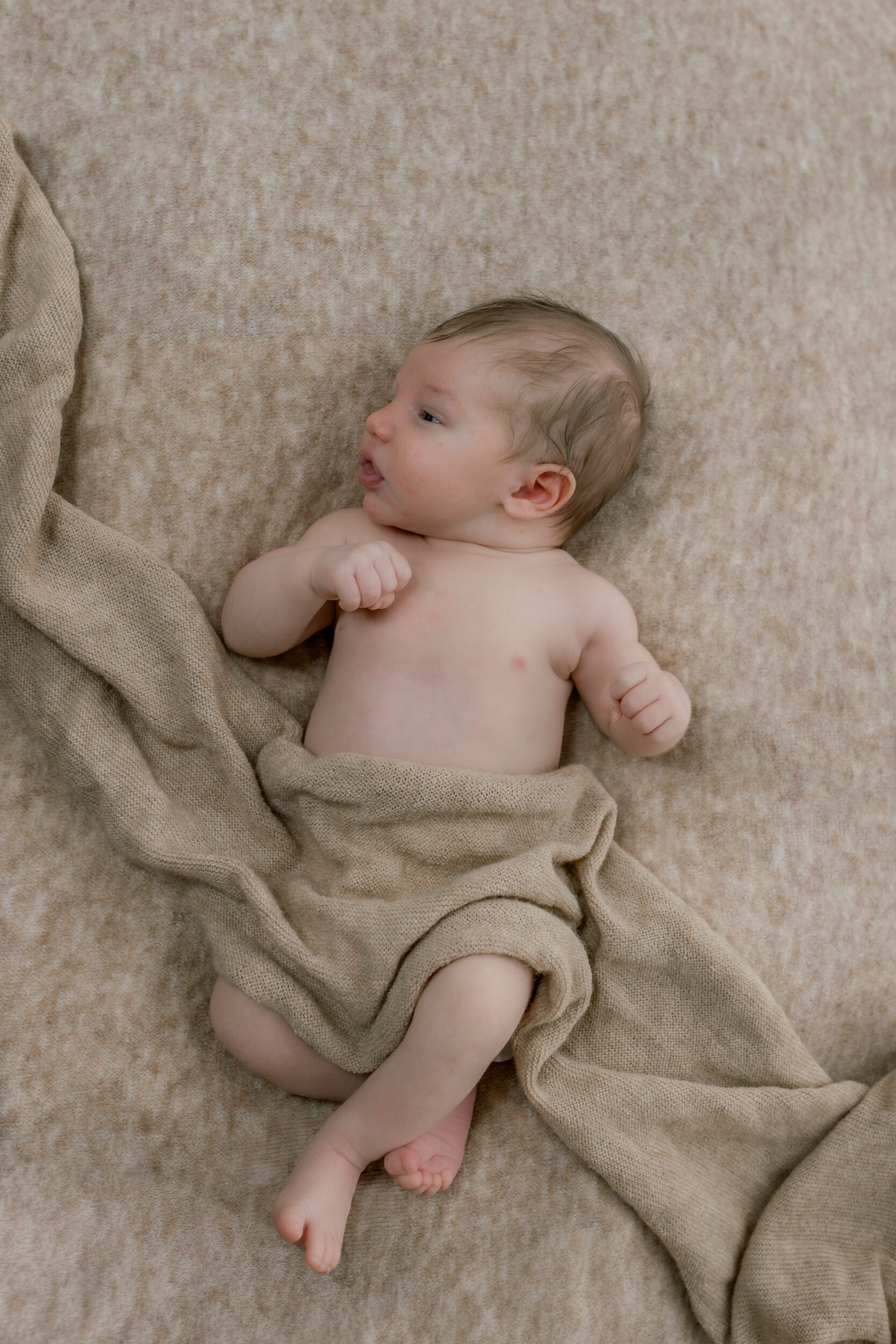 Bébé allongé sur une couverture beige.